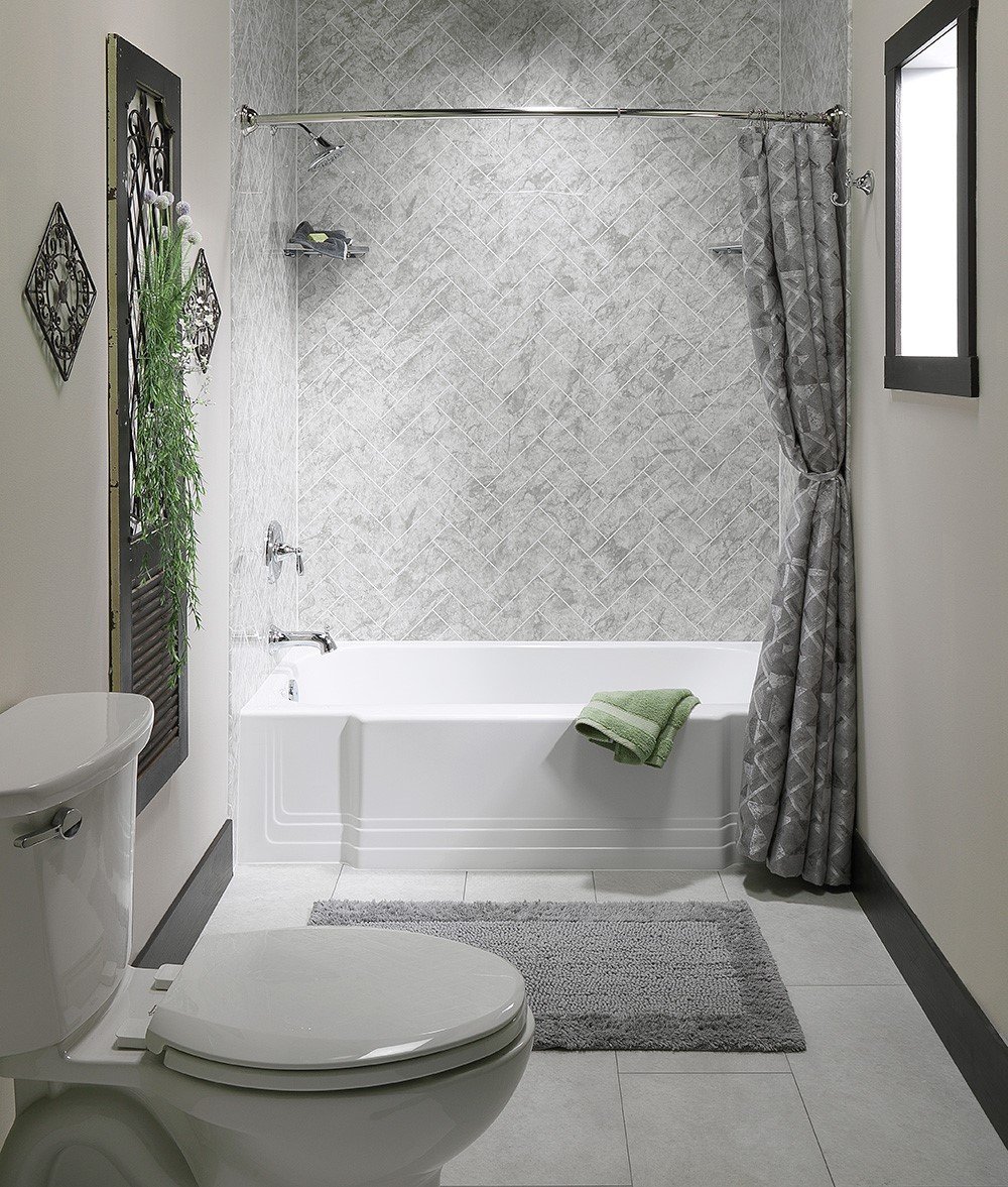 A minimalist bathroom with a white bathtub, gray herringbone tiled wall, and decorative plants.