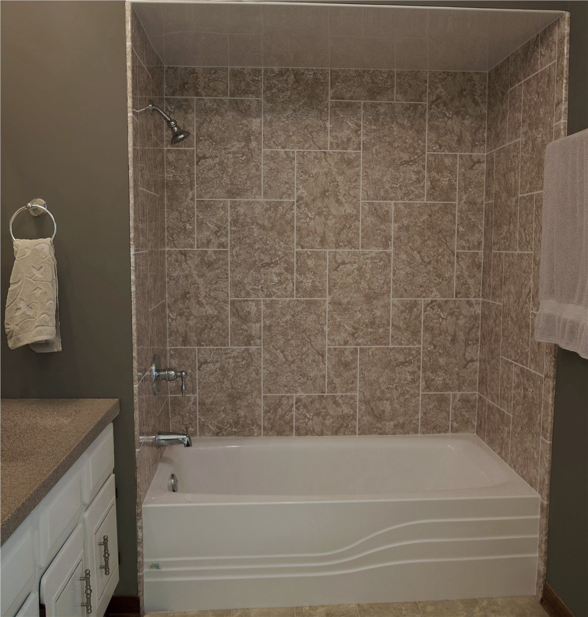 A bathroom with a white bathtub and beige geometric tiled shower wall, accented by neutral cabinetry.