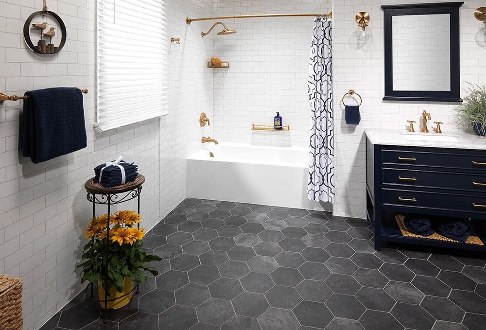 A coordinated bathroom with a white subway-tiled bathtub, gold fixtures, navy vanity, and patterned shower curtain.