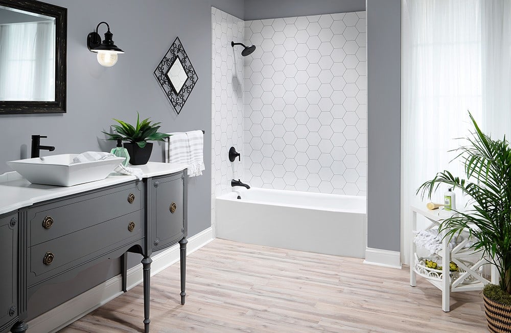 A contemporary bathroom with a gray vanity, vessel sink, hexagonal tiled bathtub wall, and decorative accents.