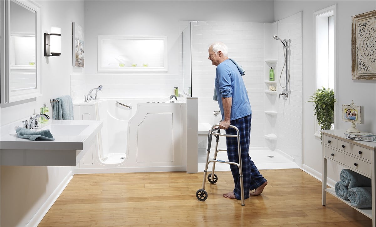 A man using a walker stands in a bathroom, highlighting accessibility features in the space.