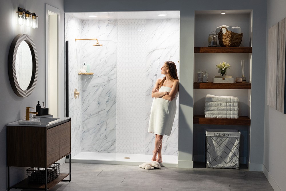 A woman stands in front of a shower in a modern bathroom, with tiles and a mirror visible in the background