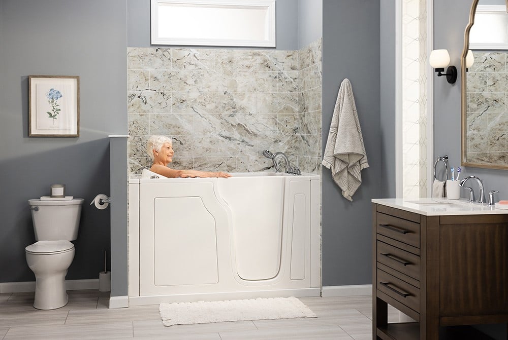An accessible bathroom with a walk-in bathtub, marble-patterned tiles, and a wooden vanity with sink.